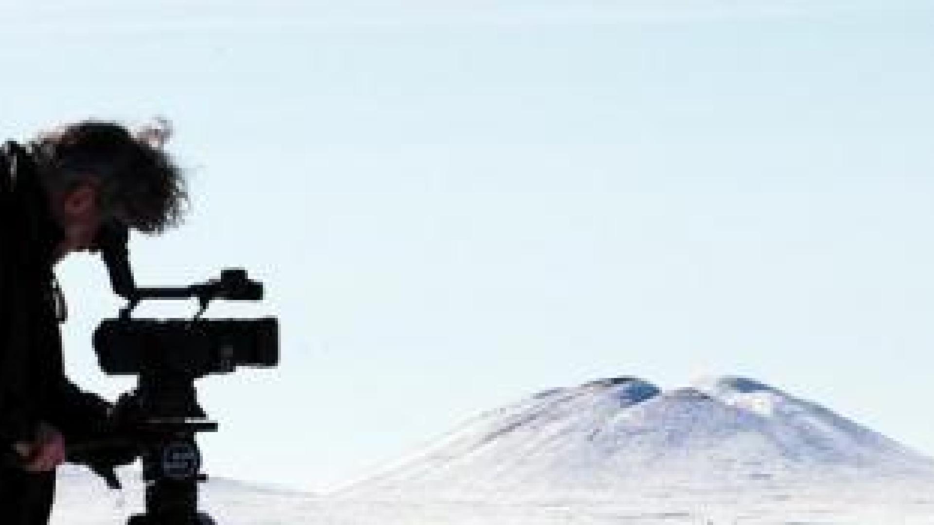 A camera operator in winter clothing filming near a pingo