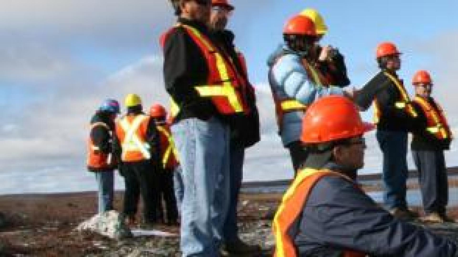 People in hard hats and safety vests observe a mine site. 